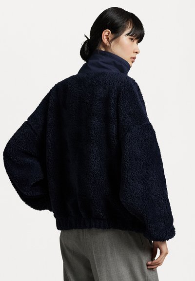 Marineblaue Fleecejacke mit strukturierter Oberfläche, oversized Passform und hohem Kragen; die Ärmelbündchen und der Saum sind elastisch für ein angenehmes Tragegefühl.