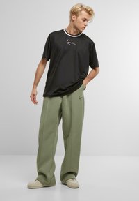 T-shirt noir à manches courtes avec logo blanc et col contrasté, associé à un pantalon large vert clair, les deux en tissu lisse.