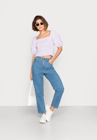 Top cropped de mangas bufantes em lavanda com textura franzida, combinado com jeans retos azuis claros e ténis brancos, acessorizado com óculos de sol.