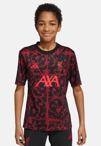 Camiseta de fútbol de manga corta en rojo y negro con patrones florales, que presenta los logotipos de "AXA" y del Liverpool FC en un brillante color rojo en la parte delantera.