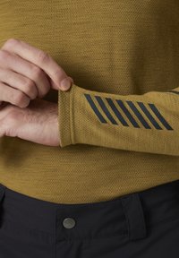 Langsleeve shirt van mosterdgele stof met een gestructureerde weving. Kenmerken van zwarte diagonale strepen op de manchetten. Zwarte broek met een metalen knoop.