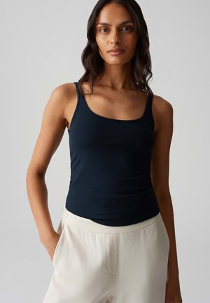 Navy Tanktop mit Rundhalsausschnitt, aus weichem Stoff. Kombiniert mit hellfarbigen, lockeren Hosen. Einfaches und figurbetontes Design.