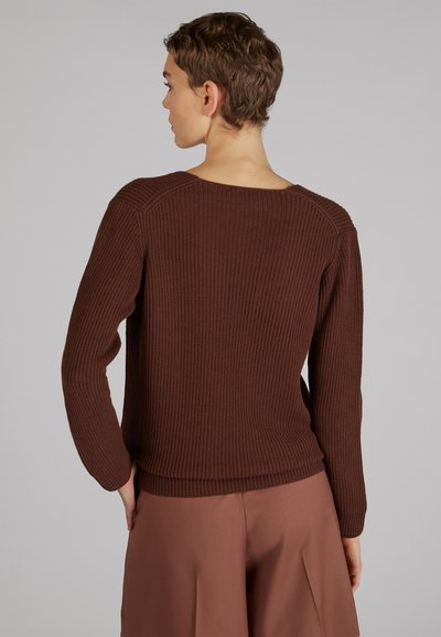Maglione marrone a costine con maniche lunghe e scollatura ampia, abbinato a pantaloni beigi a vita alta. Tessuto testurizzato e design aderente.