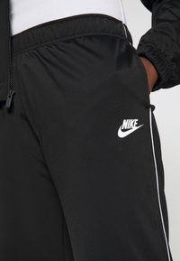 Pantaloni jogger neri realizzati in un tessuto morbido e leggero. Presentano il logo Nike in bianco, un elastico in vita e strisce laterali bianche a contrasto.