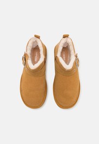 Bottines couleur tan avec un extérieur doux et texturé, doublure en fausse fourrure et détail de boucle sur le côté. Bout rond et semelle en caoutchouc robuste.