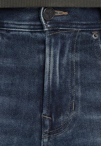 Jeans iz temno modrega denima z rahlo izblitimi teksturami, z gumbnim zapiranjem, rumenim šivanjem in podrobnostmi sprednjih žepov.