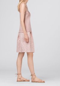 Světle růžová saténová košilka spárovaná s dlouhou sukní vzorované v jemných růžových odstínech a páskovými plochými sandály. Hladká textura a splývavý design.