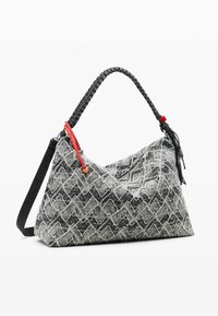 Czarna i biała torebka w wzory o teksturowanej powierzchni, z czarnym plecionym uchwytem i czerwonymi akcentami. Charakteryzuje się miękkim, trójkątnym kształtem.