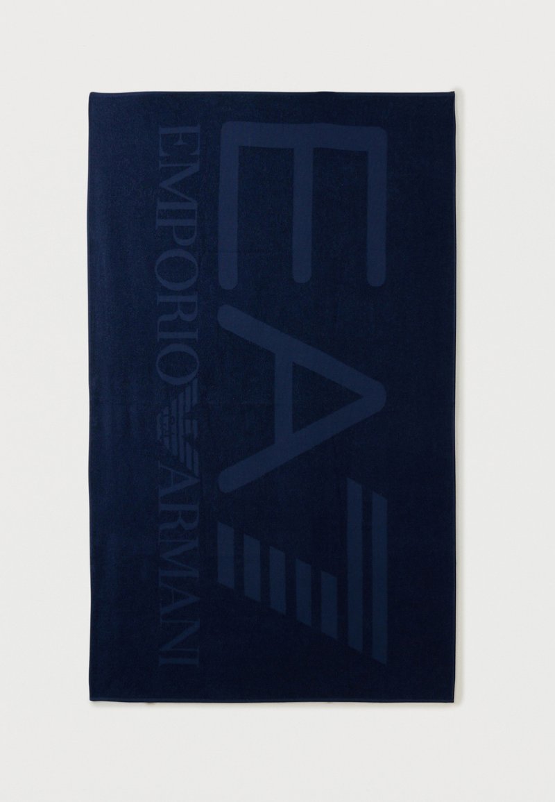 Πετσέτα ναυτικού μπλε χρώματος με μεγάλα, διακριτικά γράμματα "EA7" και λογότυπο "Emporio Armani" υφαντά κάθετα κατά μήκος της πλευράς.