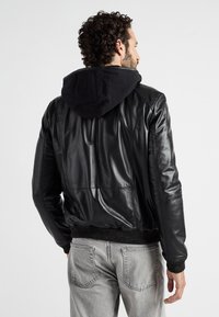 Schwarze Lederjacke mit einem schwarzen Hoodie. Verfügt über gerippte Bündchen und Saum, glatte Textur und detaillierte Nähte. Graue Jeans sichtbar.