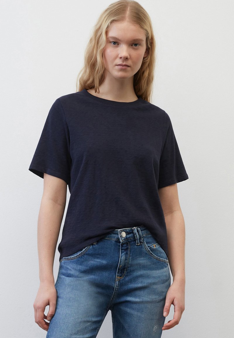 T-shirt bleu marine à manches courtes en tissu doux et texturé. Encolure ras du cou, coupe décontractée, associé à un jean en denim bleu clair.