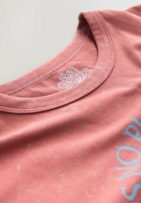 Cotton t-shirt in faded rose color with a round neckline. Features a white graphic text "The Wizard of Oz" and subtle texture details.