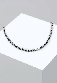 Collana in argento con maglie intrecciate, texture liscia e lucida, esposta su uno sfondo grigio chiaro.