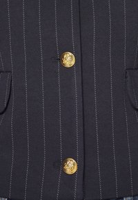 Blazer bleu marine à fines rayures avec deux boutons dorés embossés et poches à rabat de chaque côté.