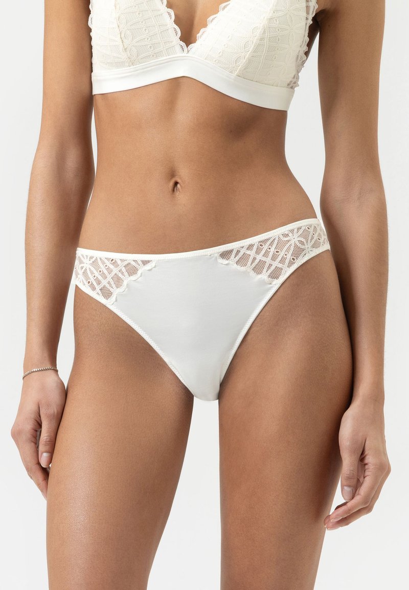 Witte kanten bikini met gaasaccenten, voorzien van een luxe tailleband en een geometrisch patroon aan de zijkanten. Zachte stof met minimale bedekking.