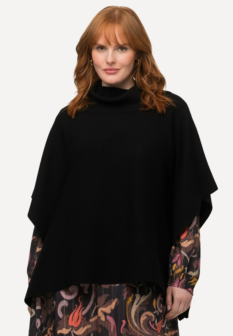 Mustapaino poncho, jossa on korkea kaulus, rento istuvuus ja sileä rakenne, yhdistettynä värikkääseen kuviolliseen mekkoon alapuolella.