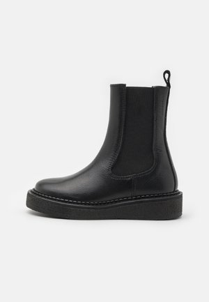Botte Chelsea en cuir noir avec panneau latéral élastique, languette de traction à l'arrière et semelle épaisse texturée, vue de profil sur fond blanc.