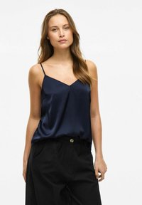 Granatowa satynowa koszulka na ramiączkach z cienkimi ramiączkami i dekoltem w kształcie litery V, w połączeniu z czarnymi spodniami o wysokim stanem z zapięciem na guzik.