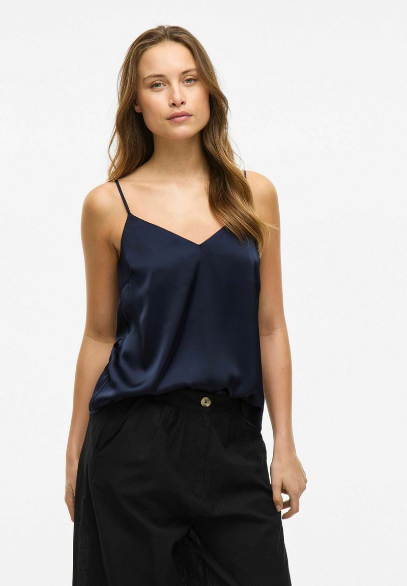 Granatowa satynowa koszulka na ramiączkach z cienkimi ramiączkami i dekoltem w kształcie litery V, w połączeniu z czarnymi spodniami o wysokim stanem z zapięciem na guzik.
