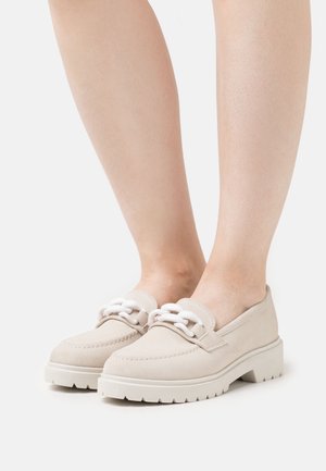 Mocasines de ante beige con cordones blancos, con una suela blanca gruesa y detalles de costura, diseñados para el uso casual.