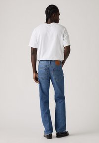 Blauwe denim jeans met een rechte pasvorm, een leren label op de achterkant van de tailleband en twee achterzakken. Gedragen met een effen wit T-shirt.