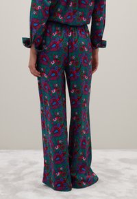 Gepaste, wijde broek in een levendige groene stof met een groot bloemen- en paisleypatroon in rood, blauw en wit, met een gladde textuur.