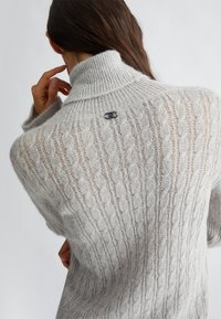 Maglione lavorato a maglia grigio chiaro con colletto a coste, motivo a trecce e un piccolo accento di logo argentato nella parte superiore della schiena.