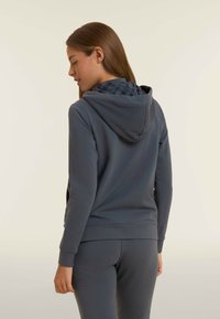 Felpa grigia scura con cappuccio a fantasia. Realizzata in morbido tessuto, presenta una vestibilità comoda e polsini a coste. Abbinate a pantaloni coordinati.