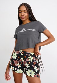 T-shirt grigia corta con design a onde bianche e testo "ROXY", abbinata a pantaloni corti neri con fiori e accenti verdi, arancioni e marroni.