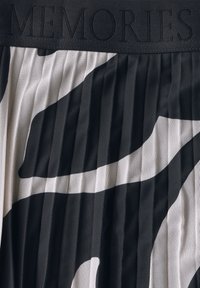 Tessuto plissettato in bianco e nero con una stampa animale audace. Presenta una vita piatta impressa con la scritta "MEMORIES". Materiale testurizzato e traspirante.