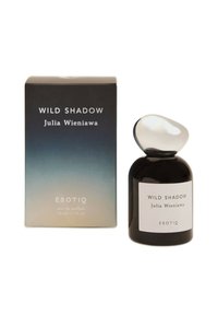Czarna szklana butelka perfum z zaokrągloną nakrętką, oznaczona etykietą "WILD SHADOW", obok gradientowego pudełka o kolorach od jasnoniebieskiego do ciemnego zielononiebieskiego z białym napisem.