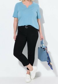 Světle modré tričko s výstřihem do V v kombinaci s černými úzkými džíny a bílými teniskami. Nese světle modrou kabelku s barevným šátkem.