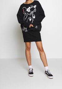 Sudadera negra con un diseño gráfico blanco, combinada con una falda vaquera negra. La persona lleva zapatillas negras y calcetines blancos.