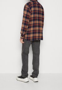 Langarm geruite shirt met rode, blauwe en gele patronen, gecombineerd met donkergrijze jeans en zwarte sneakers met witte zolen.