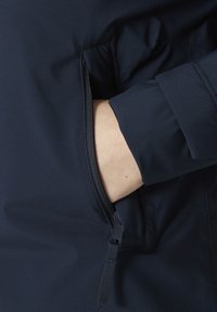 Chaqueta impermeable de color marino con textura suave, que presenta un bolsillo lateral con cremallera y un diseño de puños doblados.