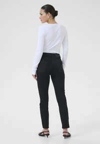 Pantalons noirs taille haute à coupe slim, avec deux poches arrière, associés à un haut à manches longues en tissu côtelé de couleur blanche.