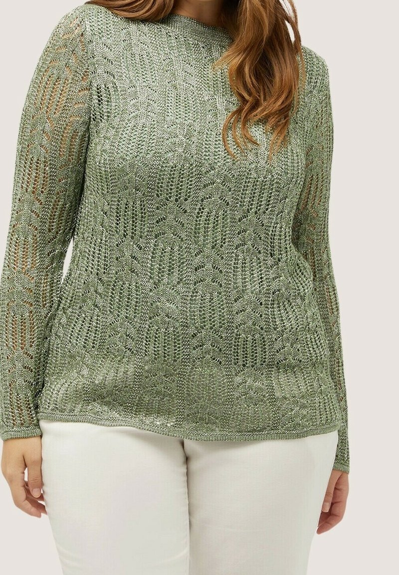 Pull en maille vert clair à manches longues, présentant un motif ajouré. Col et poignets soulignés, assortis à un pantalon blanc.