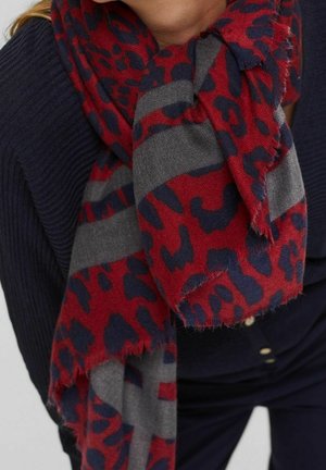 Personne portant un pull côtelé bleu marine avec une grande écharpe à imprimé animal rouge et bleu marine avec des rayures grises, nouée autour du cou.