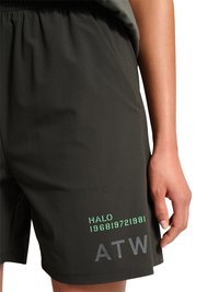 Zwarte shorts met groene "HALO 196819721981" en grijze "ATW" tekst op het been, gedragen door een persoon met de arm ontspannen langs het lichaam.