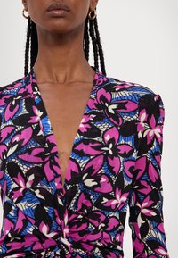 Blommig blus med djup V-hals och twistdetalj. Livfulla rosa och blå blommönster på svart bakgrund; texturerad tyg.