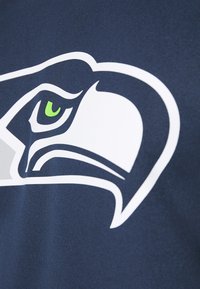 Tessuto blu navy con un grande logo bianco e verde dei Seattle Seahawks, che mette in evidenza la testa e l'occhio dell'uccello in un design prominente.