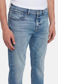 Jeans in denim azzurro chiaro con una vestibilità slim, caratterizzati da un classico design a cinque tasche, leggere sfumature e dettagli in metallo color ottone.