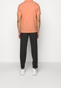 Lyhythihainen persikkavärinen polo-paita yhdistettynä tummanharmaisiin housuihin, joissa on rento malli ja valkoiset lenkkarit. Silkkinen kangas ja siistit linjat.