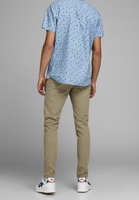 Light blue short-sleeve shirt with a dark pattern, paired with tan slim-fit pants and white sneakers featuring black and red accents.