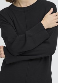 Must pullover-kampsun soonelise kaeluse ja mansettidega, mugava istuvuse ja esiküljel ning varrukatel õmmeldud detailidega.