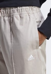 Ljust beige avslappnade byxor med elastisk midja och sidofickor. Har en vit Adidas-logotyp broderad på vänster ben.