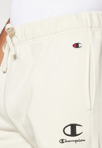 Pantalons de survêtement crème clair en tissu doux, dotés d'un cordon de serrage réglable, de poches latérales et d'accents brodés au logo Champion.