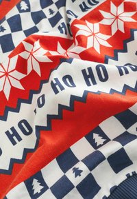 Röd, vit och blå mönstrad tröja med snöflingor, träd och texten "HO HO HO", med en stickad struktur och zickzack-detaljer.