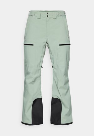 Lichtgroene waterdichte broek met zwarte accenten, ritszakken, een knoop- en haaksluiting, en verstelbare functies bij de enkels.