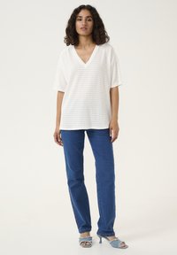 White V-neck T-shirt with a textured pattern, paired with blue straight-leg jeans and light blue heeled sandals.